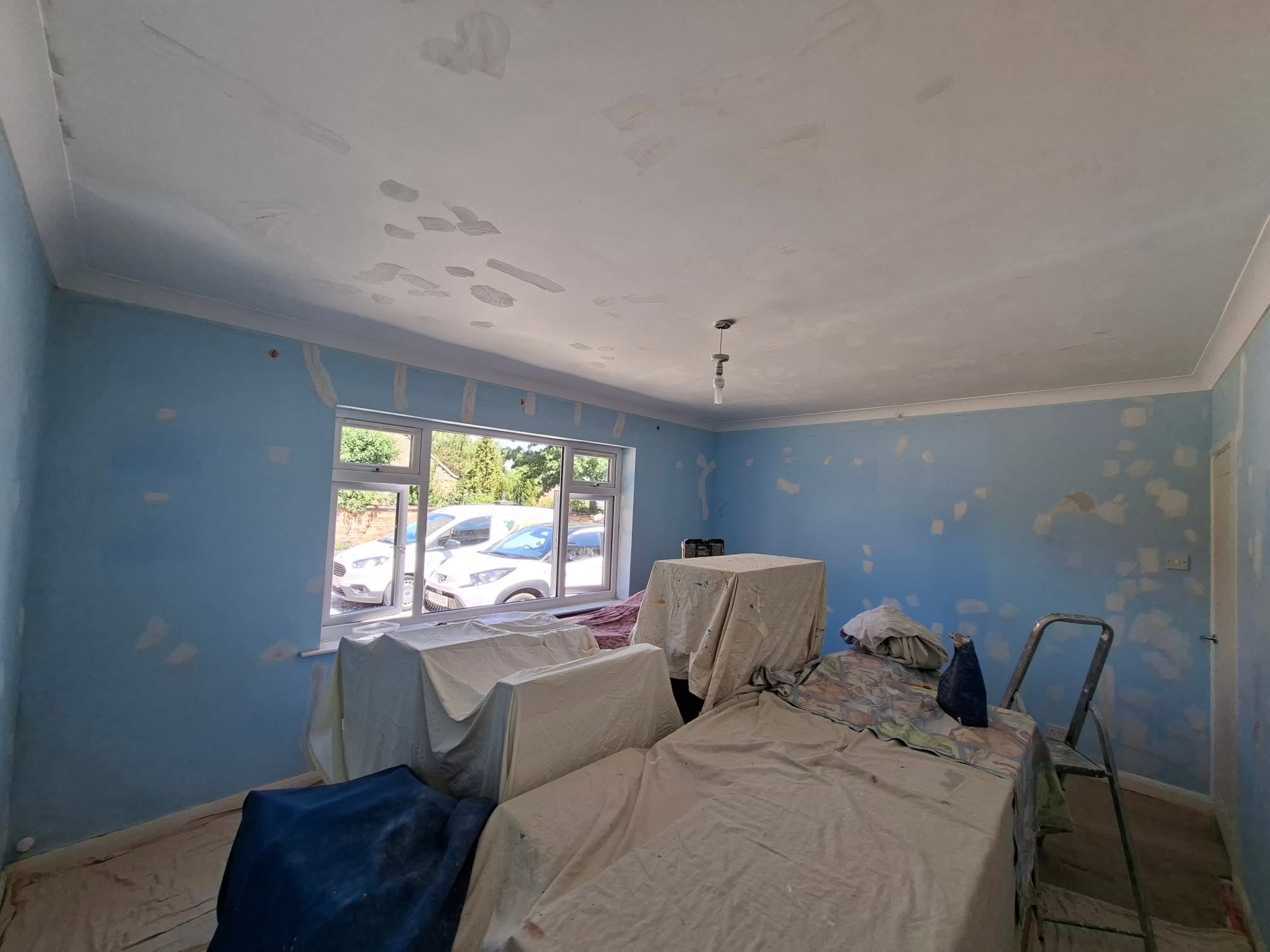 Bedroom before decorating: blue walls and ceiling covered in filler patches, furniture under dust sheets