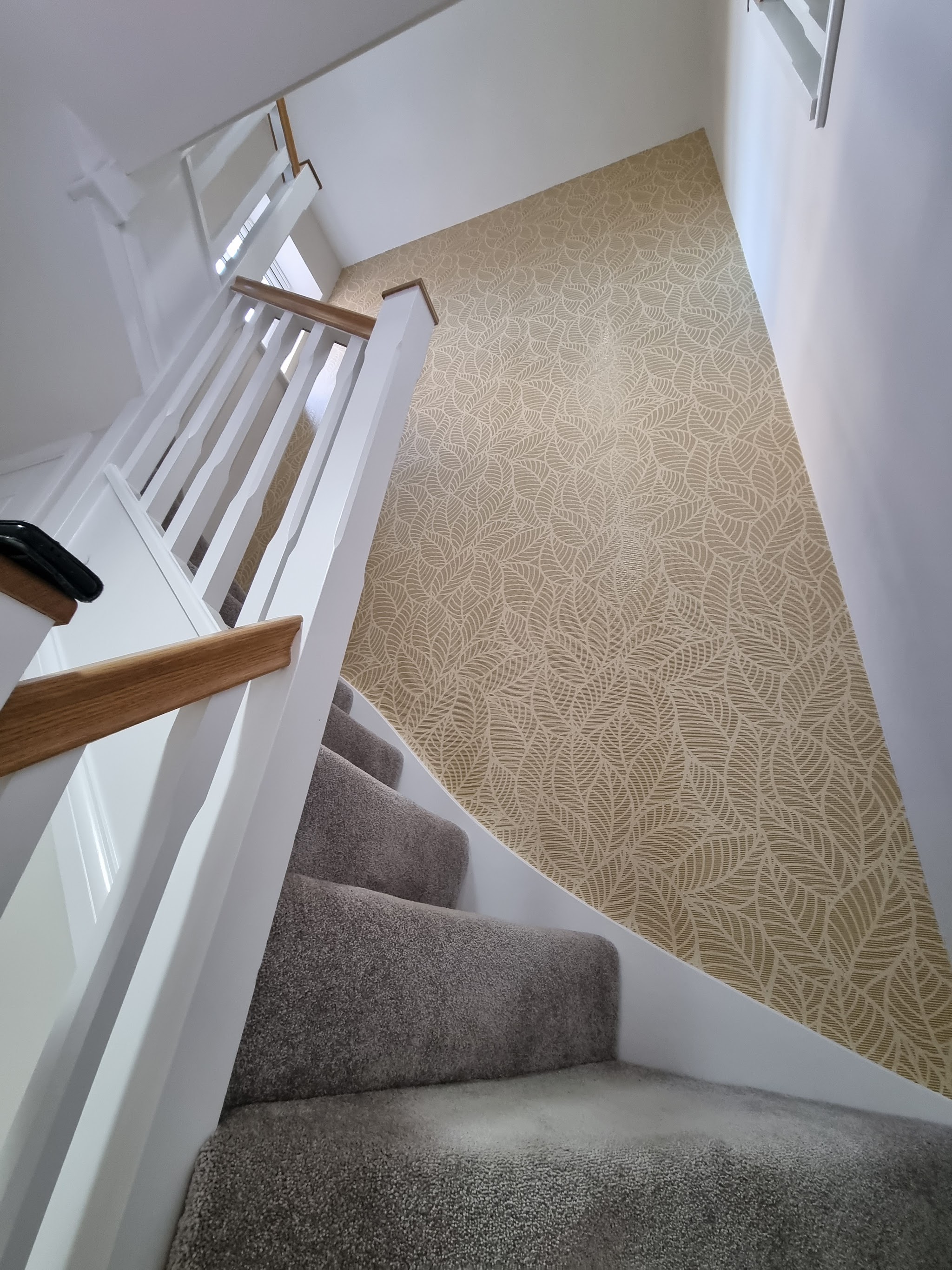 Staircase seen from above, with leaf pattern wallpaper on the stair wall, white spindles and an oak handrail