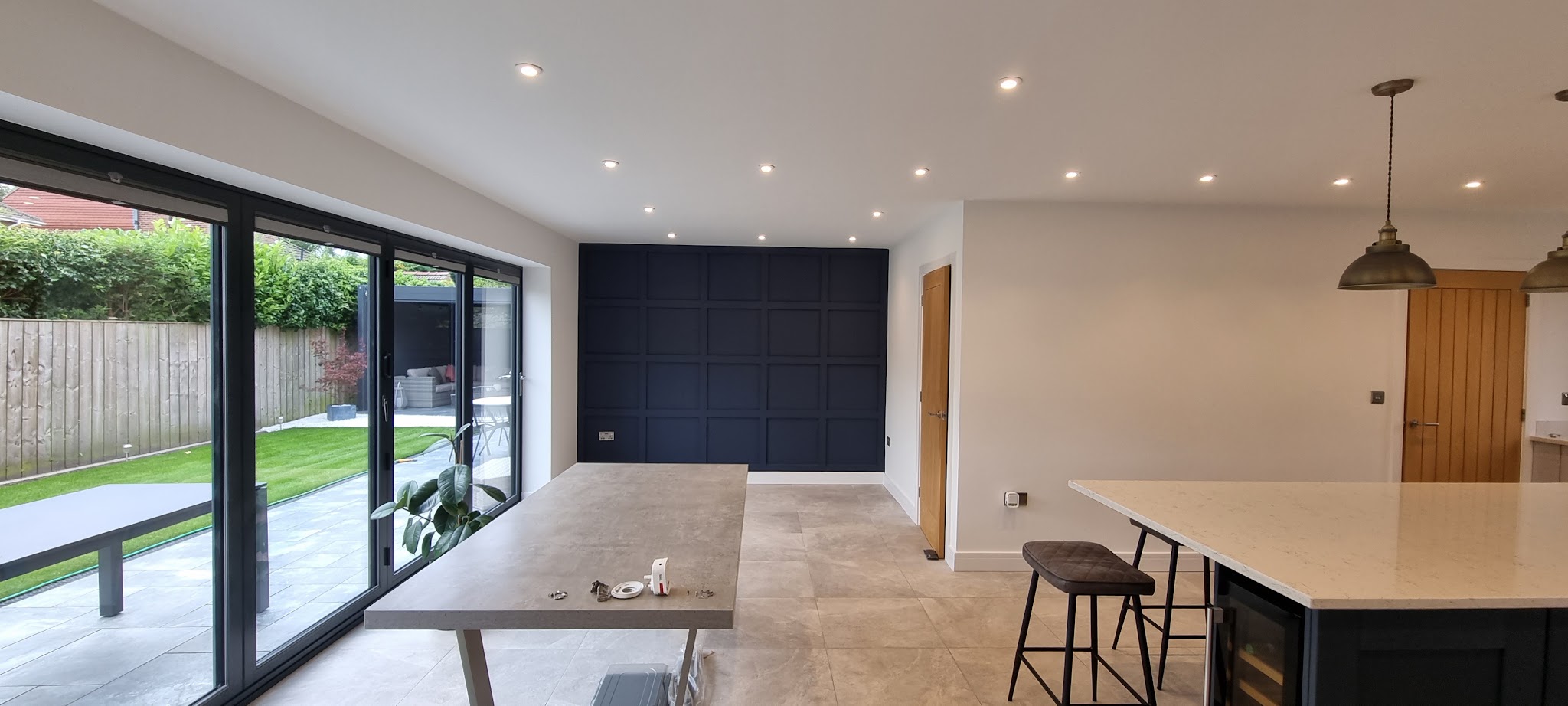 Open plan kitchen with white walls, a navy panelled feature wall and bifold doors to the garden