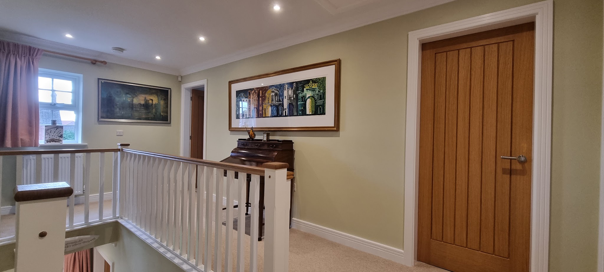 Landing with pale olive walls, a white balustrade and an oak door