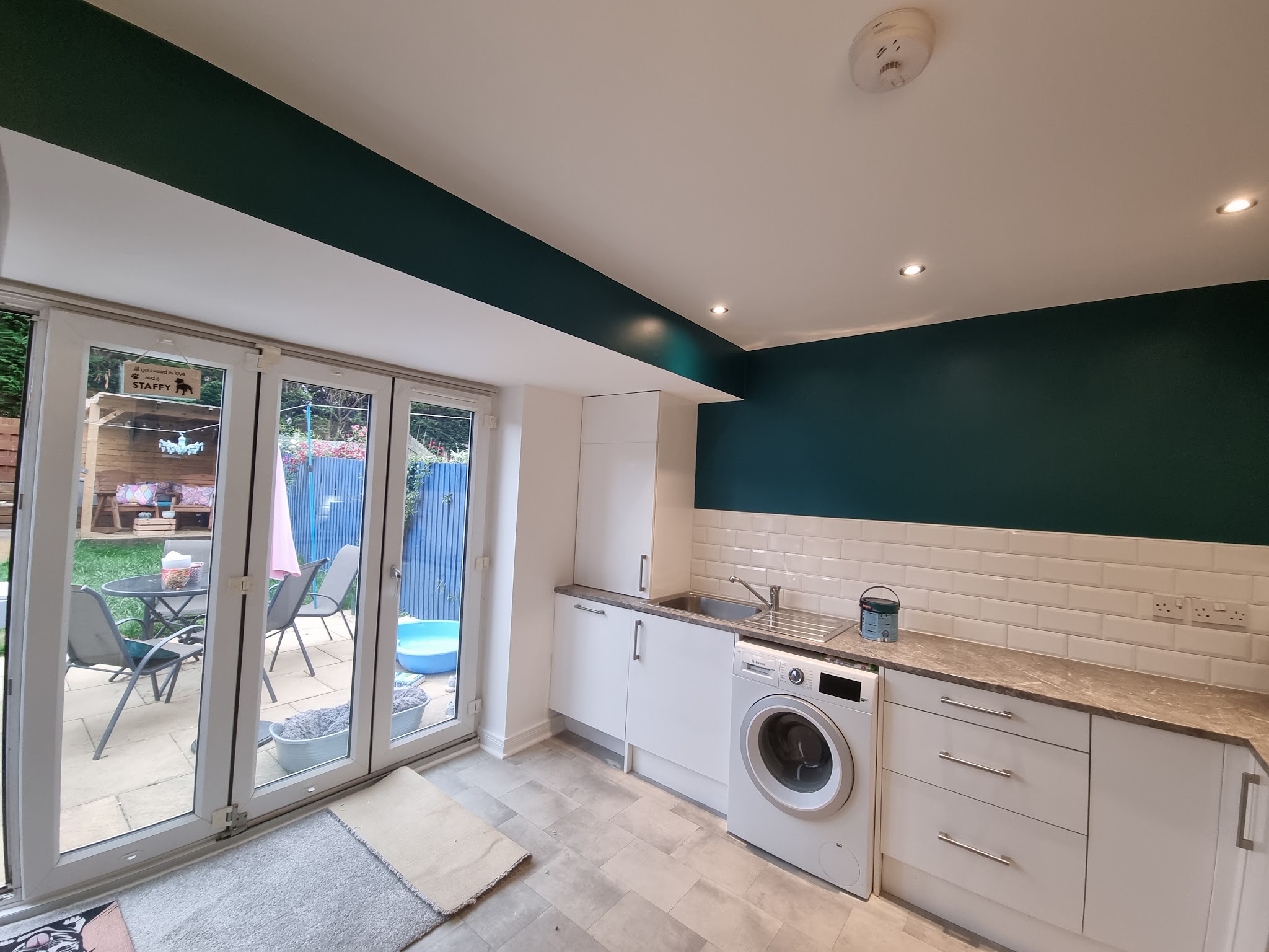 Kitchen with deep teal walls above white metro tiles and French doors to a patio