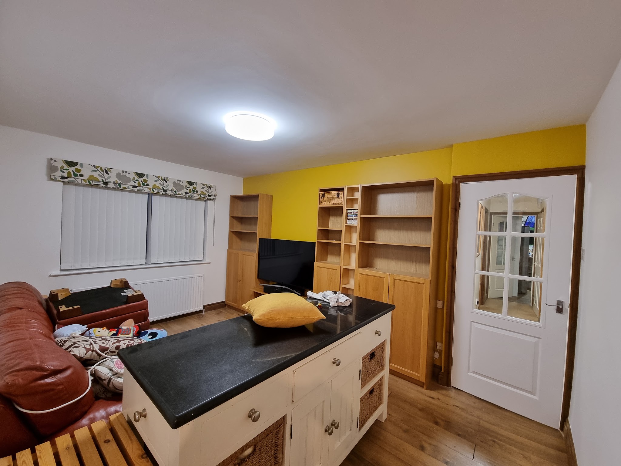 Kitchen and living room with a mustard yellow feature wall and oak shelving